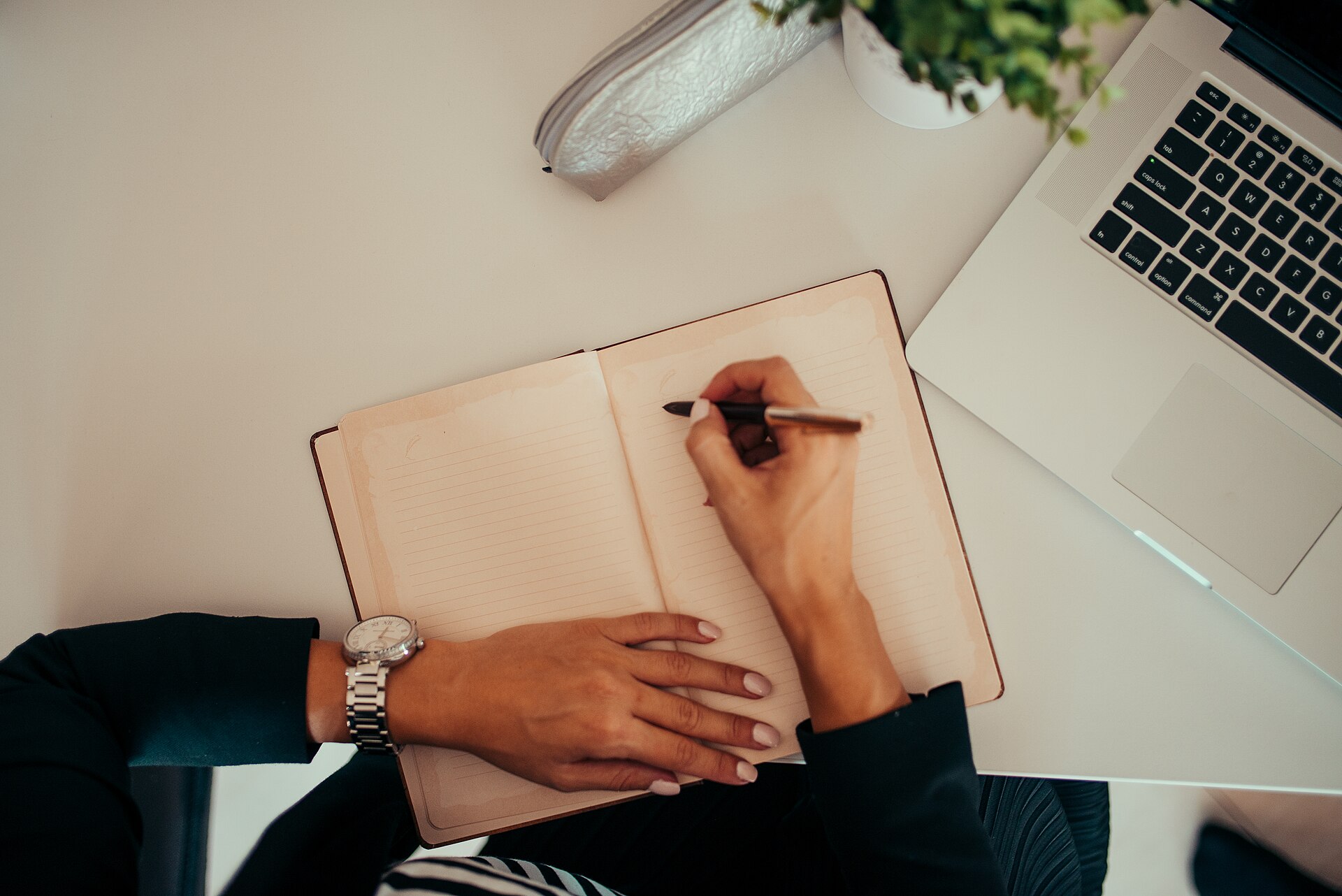 Writing in a notebook beside a laptop